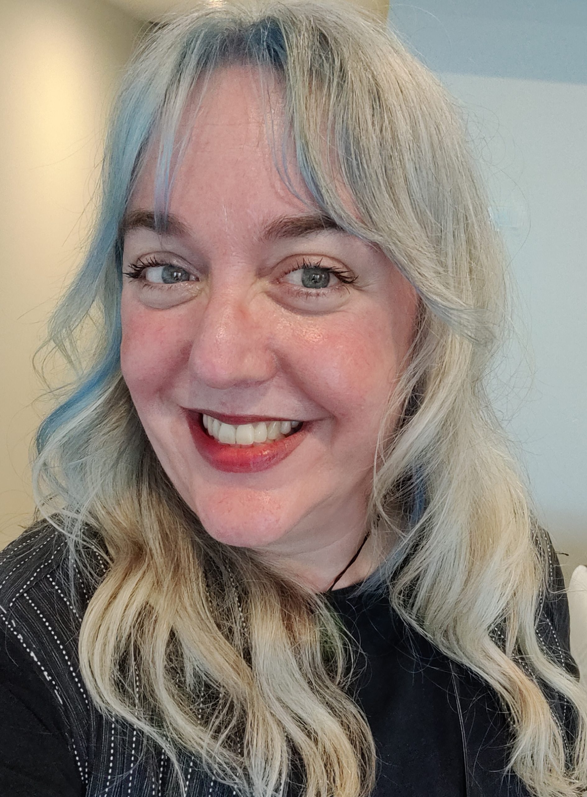 Rachael Herron, a white woman with blue eyes, silver hair with blue streaks, wearing a black shirt, smiling